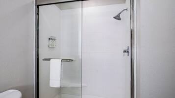 A glass-enclosed shower with a handheld showerhead, a white towel on a rack, and a white toilet visible to the left.