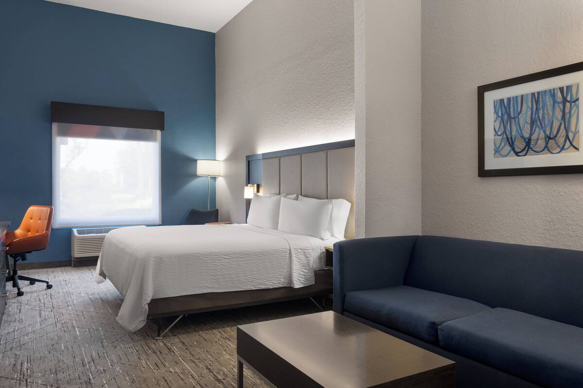 A hotel room with a bed, a blue sofa, a desk, and a chair.