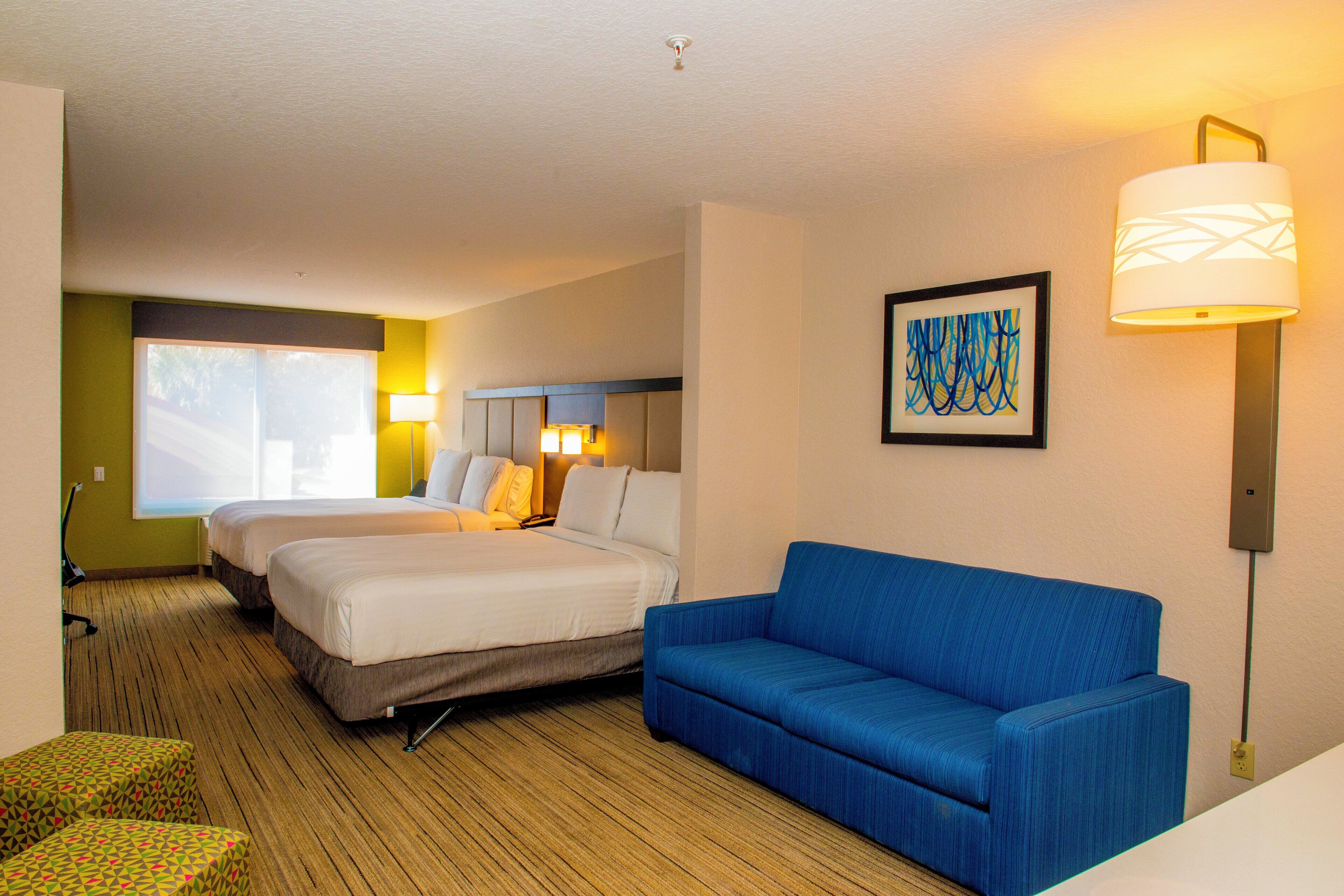 A hotel room with two beds, a blue sofa, a painting, and a lamp.
