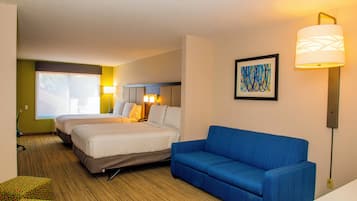 A hotel room with two beds, a blue sofa, a painting, and a lamp.