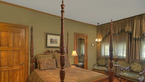 Une chambre à coucher de style traditionnel, avec un lit à baldaquin, deux fauteuils, une armoire en bois et un miroir.