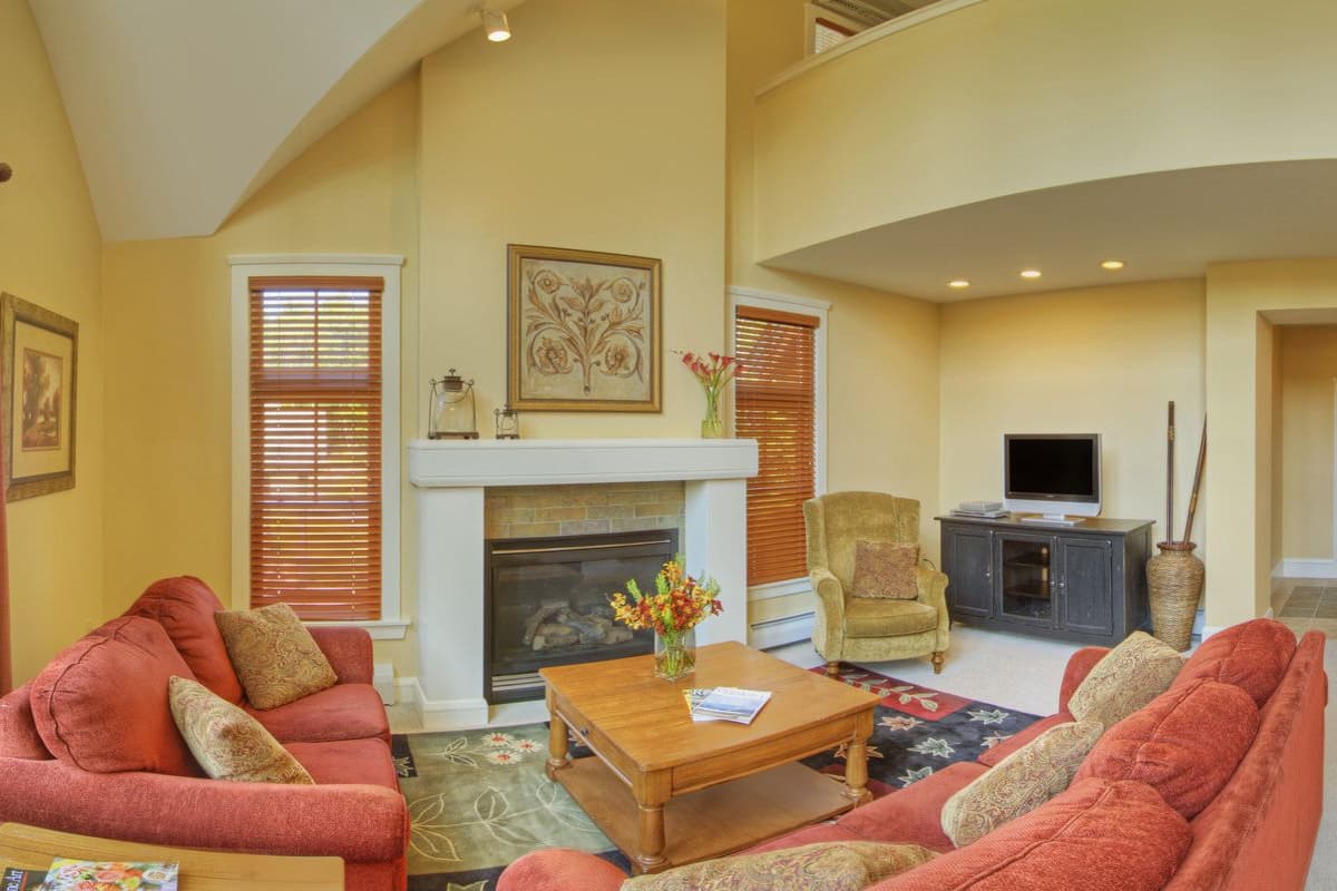 Un salón espacioso con chimenea, sofás rojos, una mesa de centro de madera y un televisor.