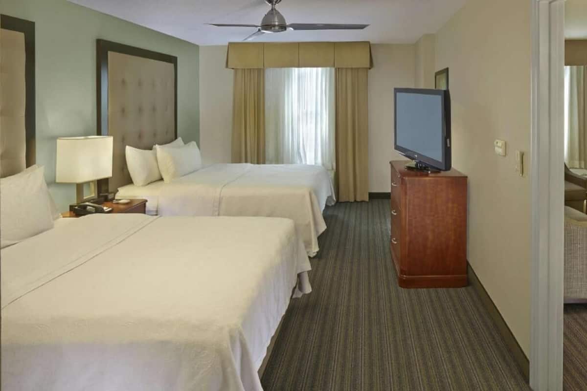 A hotel room with two beds, a television, a ceiling fan, and a window with curtains.