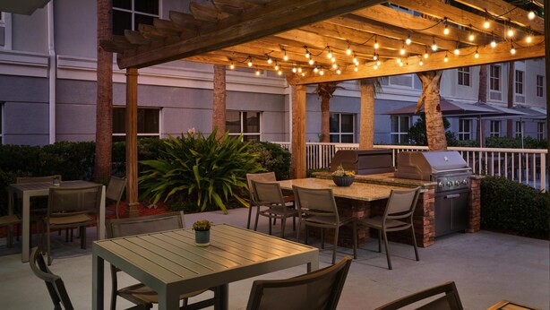 An outdoor patio with a wooden pergola, string lights, a barbecue grill, and seating arrangements. - Homewood Suites by Hilton Daytona Beach Speedway-Airport (Daytona Beach)