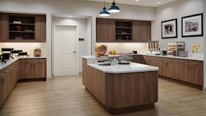 A modern kitchen with wooden cabinets, a central island, pendant lighting, and a refrigerator. - Homewood Suites by Hilton Daytona Beach Speedway-Airport (Daytona Beach)