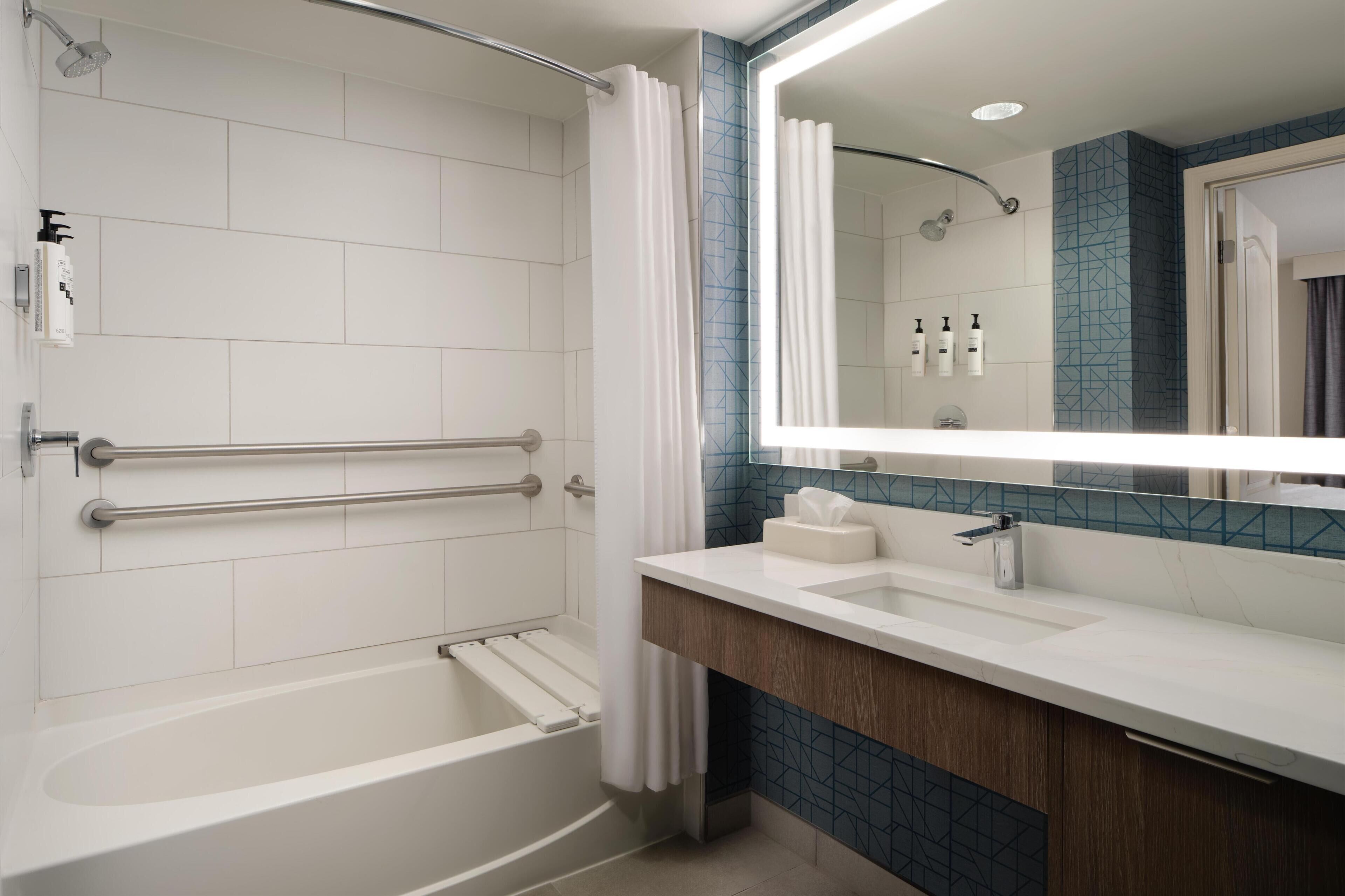 A modern bathroom with a bathtub, a shower, a vanity with a mirror, and a towel rack.