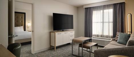 Habitación de hotel con cama, televisor, sofá, una mesita y ventana con cortinas.