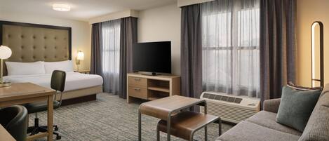 A hotel room with a bed, desk, chair, TV, and a sofa.