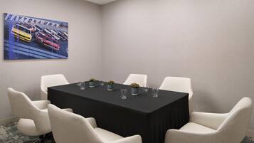 A conference room with a black table, white chairs, and a painting of racing cars on the wall.