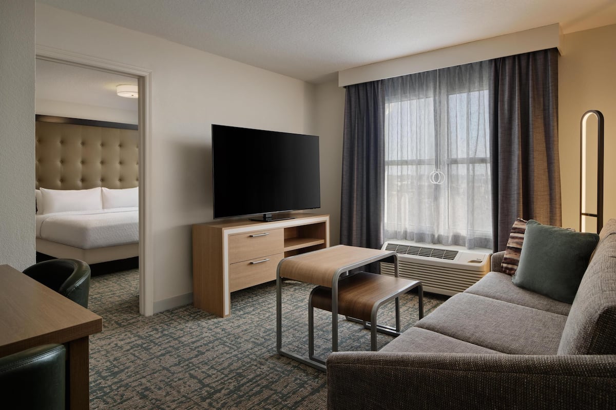 A hotel room with a bed, a TV, a sofa, a desk, and a window with curtains.