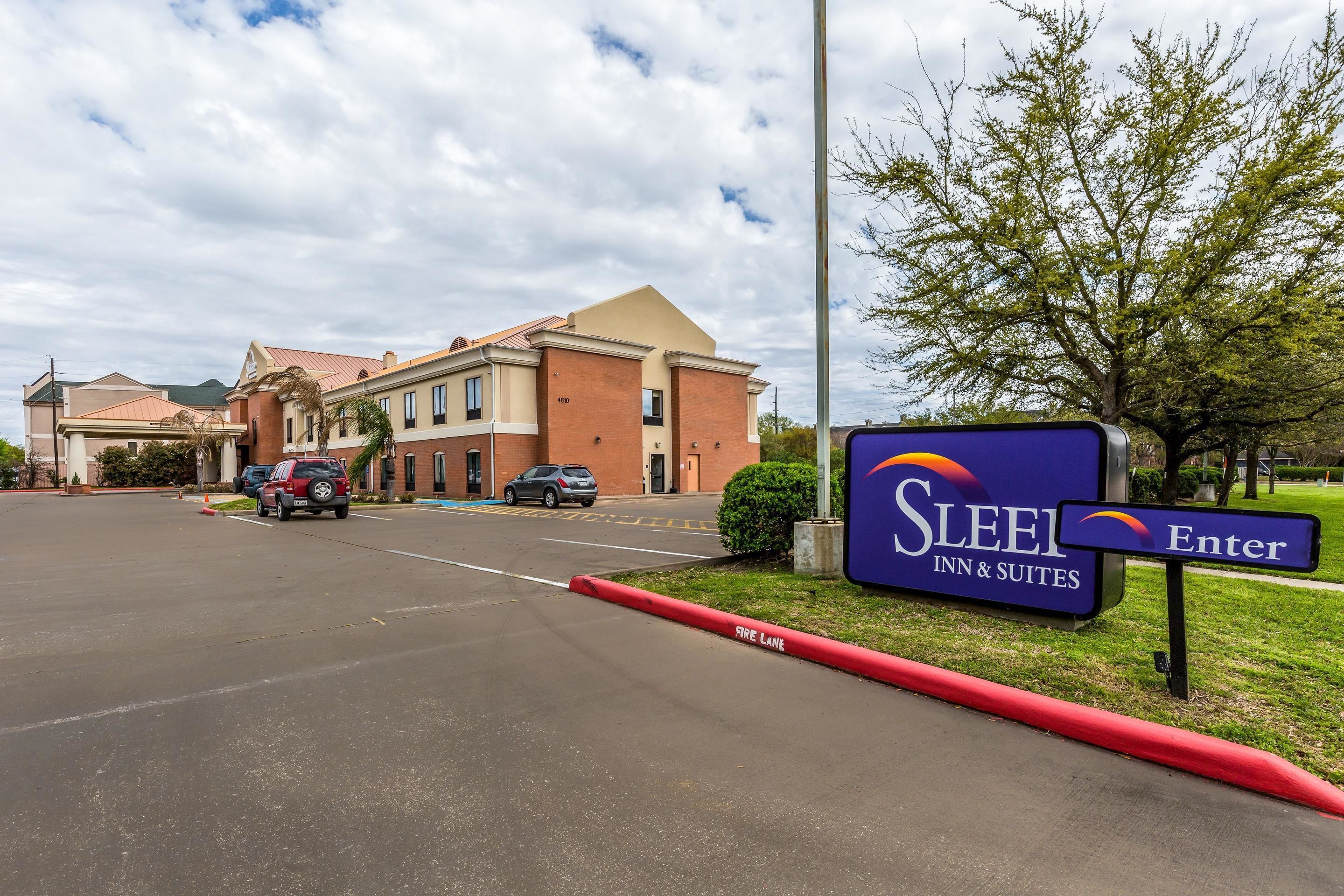A parking lot with a 'Sleigh Inn & Suites' sign, a building with a brick facade, and a red curb.