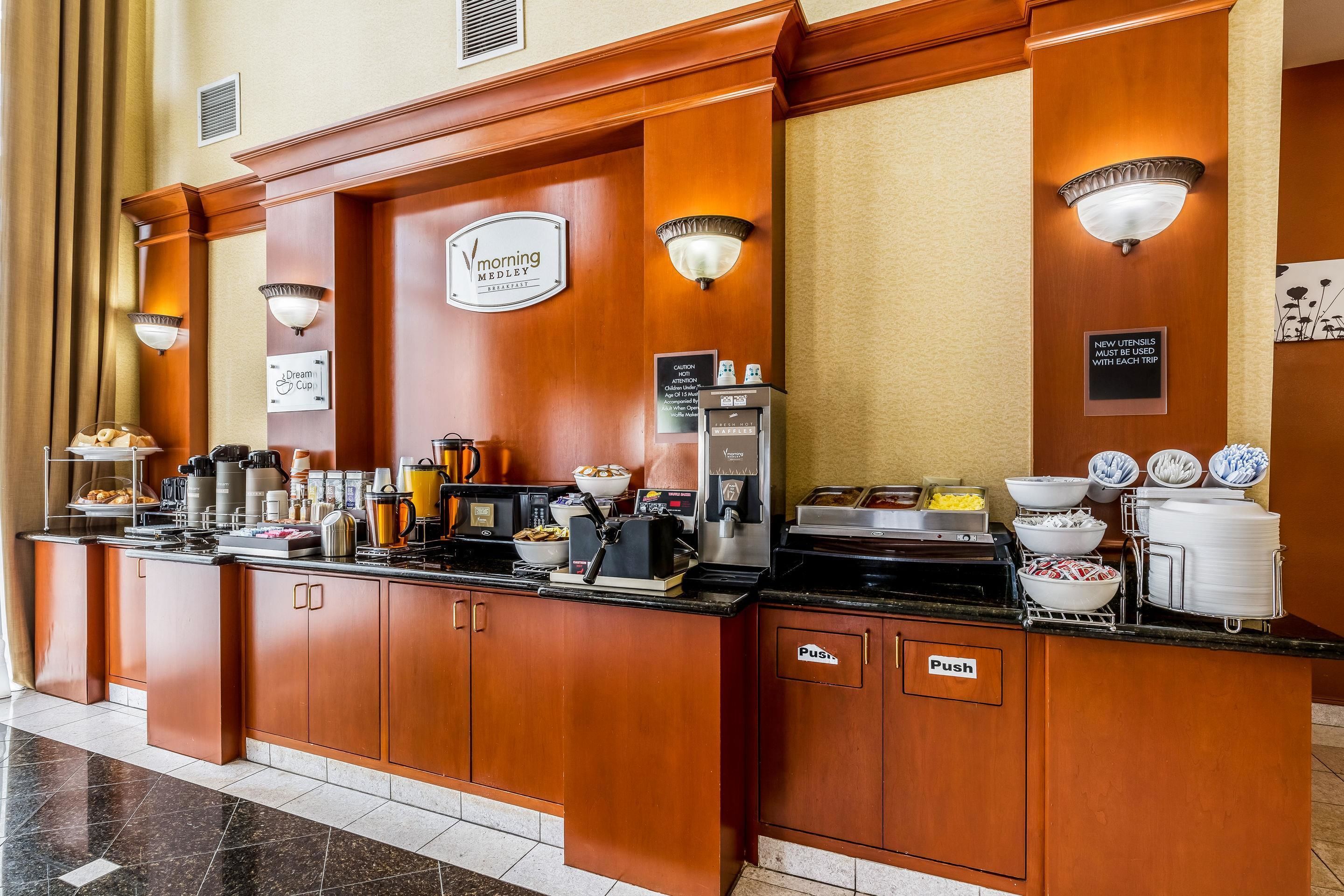 Zona de recepción de hotel con una estación de café, un cartel que dice 'Morning Medley' y un letrero que indica 'Utensilios Nuevos'.