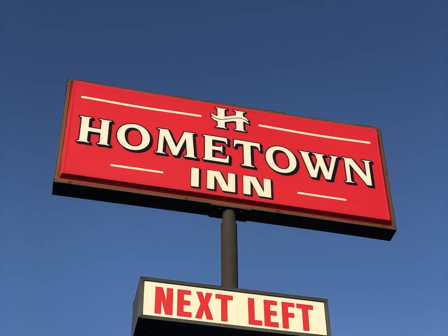 Schild für das Hometown Inn, darunter ein Wegweiser mit der Aufschrift 'Nächster Abbiegepfeil links'.