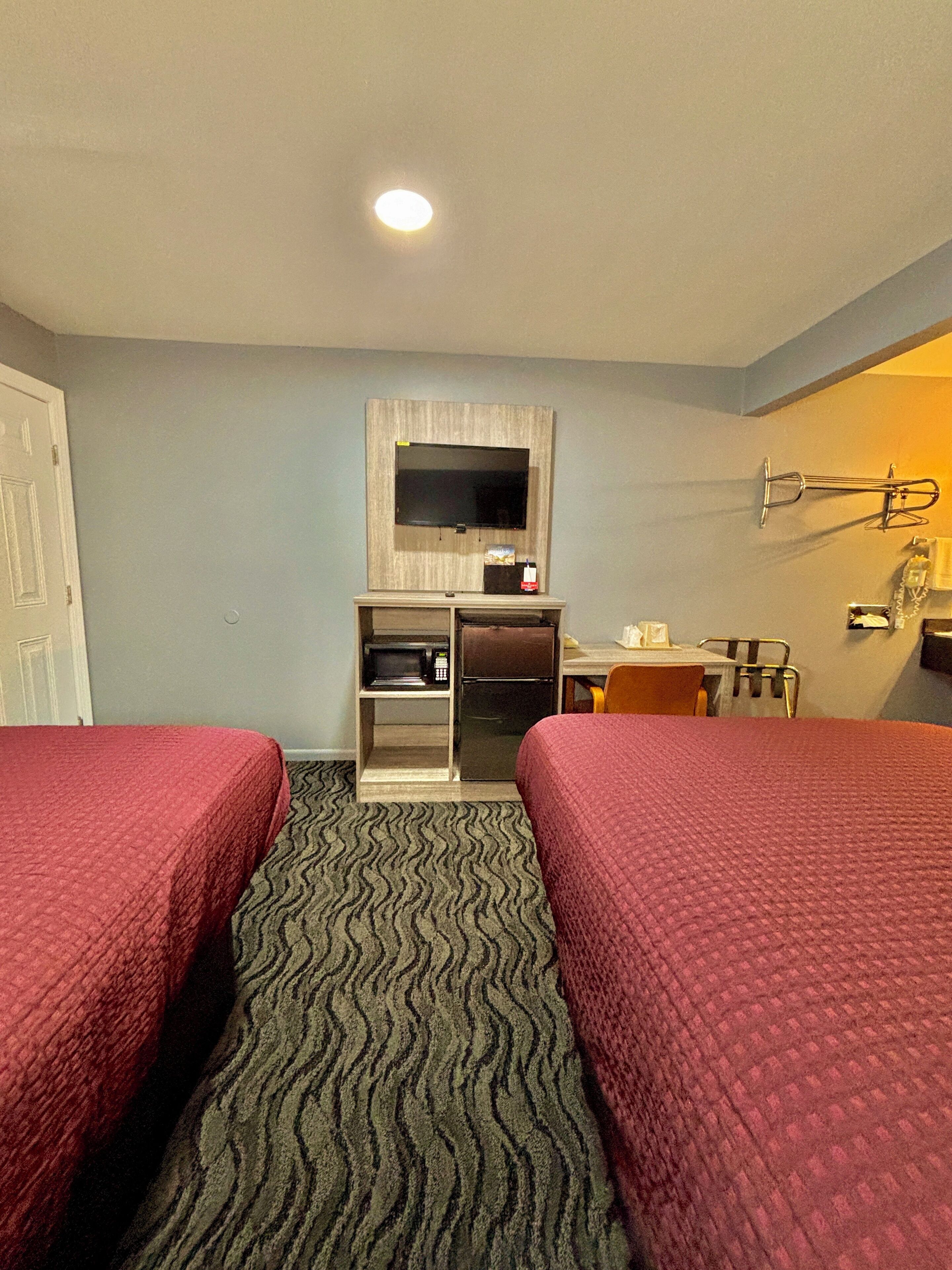 Habitación de hotel con dos camas, un televisor en la pared, un refrigerador, un microondas, un escritorio y una silla.