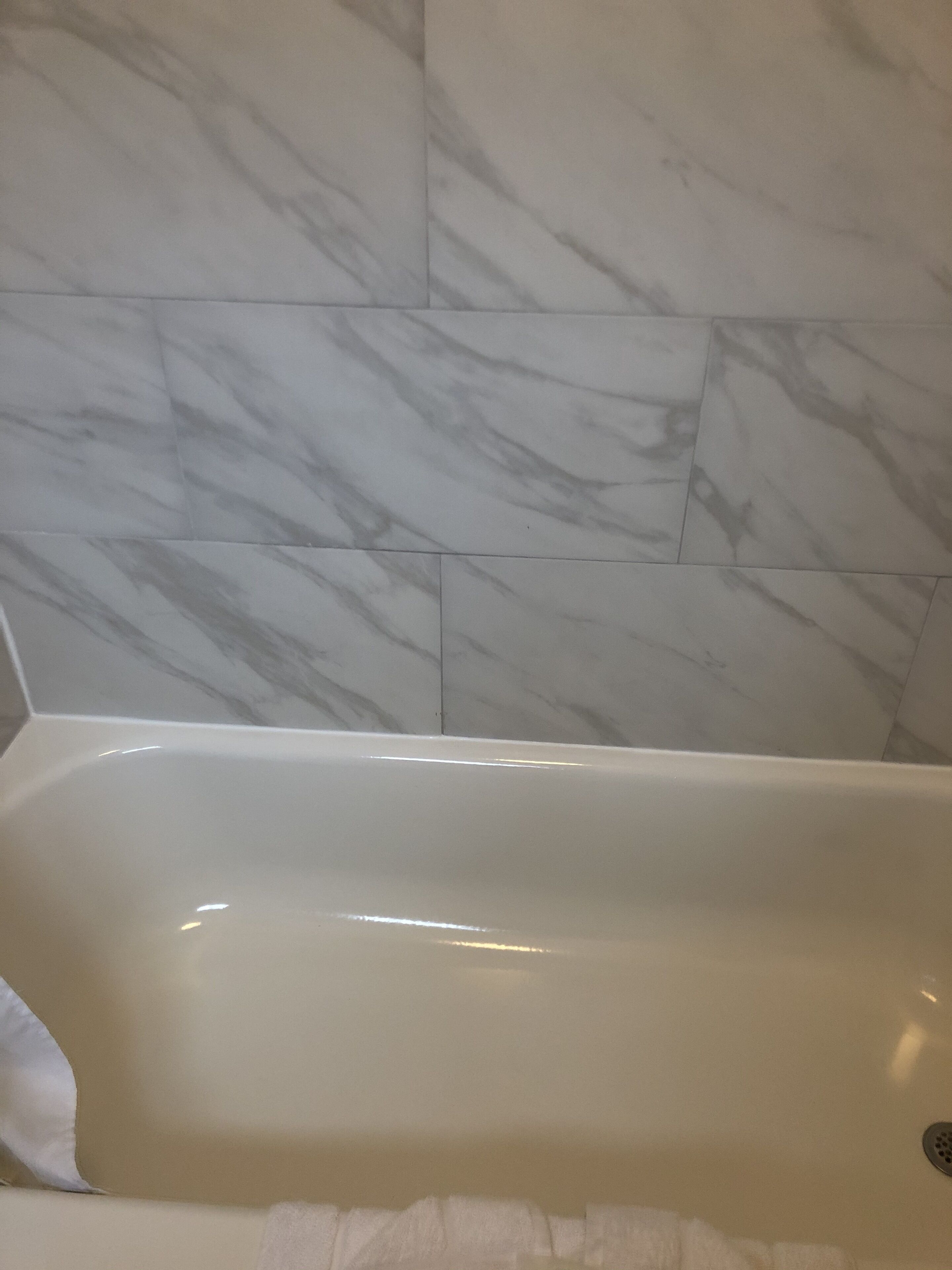 Una bañera con interior blanco, junto a una pared con baldosas de mármol.
