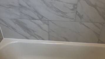 Una bañera con interior blanco, junto a una pared con baldosas de mármol.