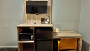 Ein kleines Hotelzimmer mit einem Holztisch, einem Fernseher, einem Kühlschrank und einem einzelnen Sessel.