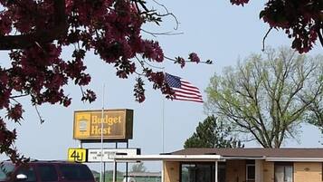 A Budget Host hotel with an American flag, a parking sign, and a maroon SUV.