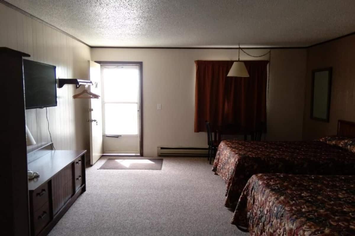 A hotel room with a bed, a desk, a TV, and a window with curtains.