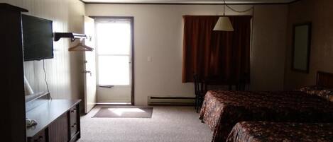 Habitación de hotel con cama, escritorio, televisión y ventana con cortinas.