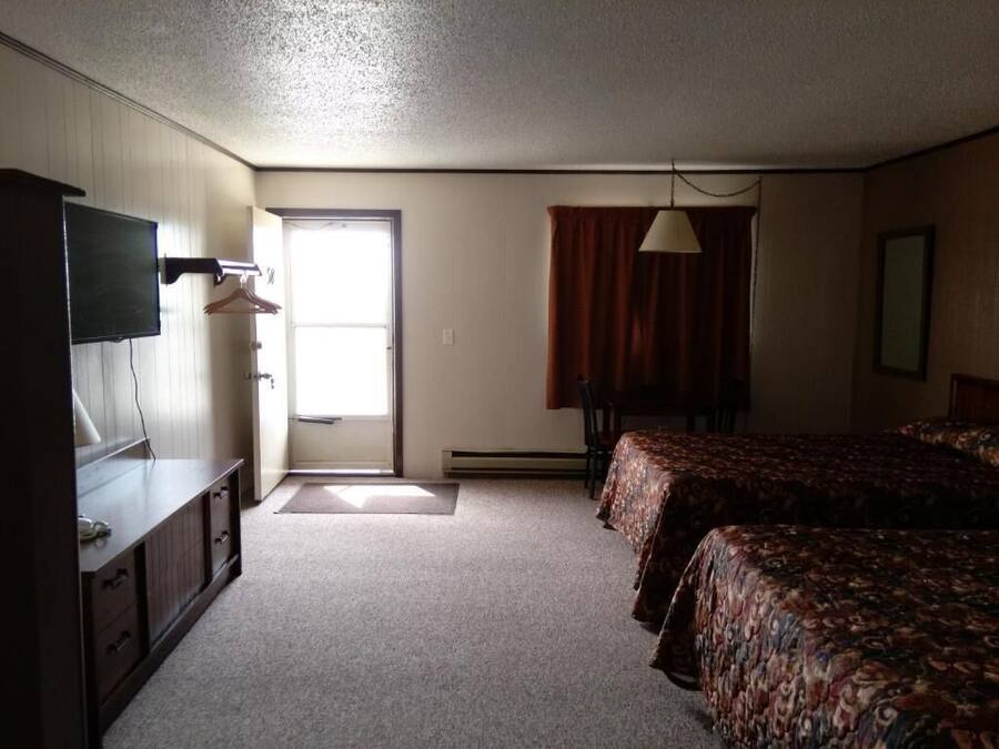 Habitación de hotel con cama, escritorio, televisión y ventana con cortinas.