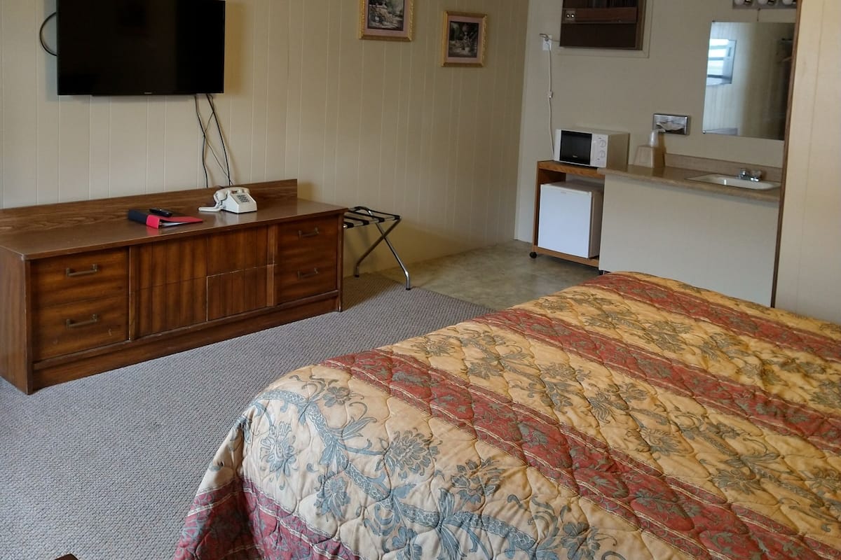 A bedroom with a bed, dresser, television, and a small kitchenette.