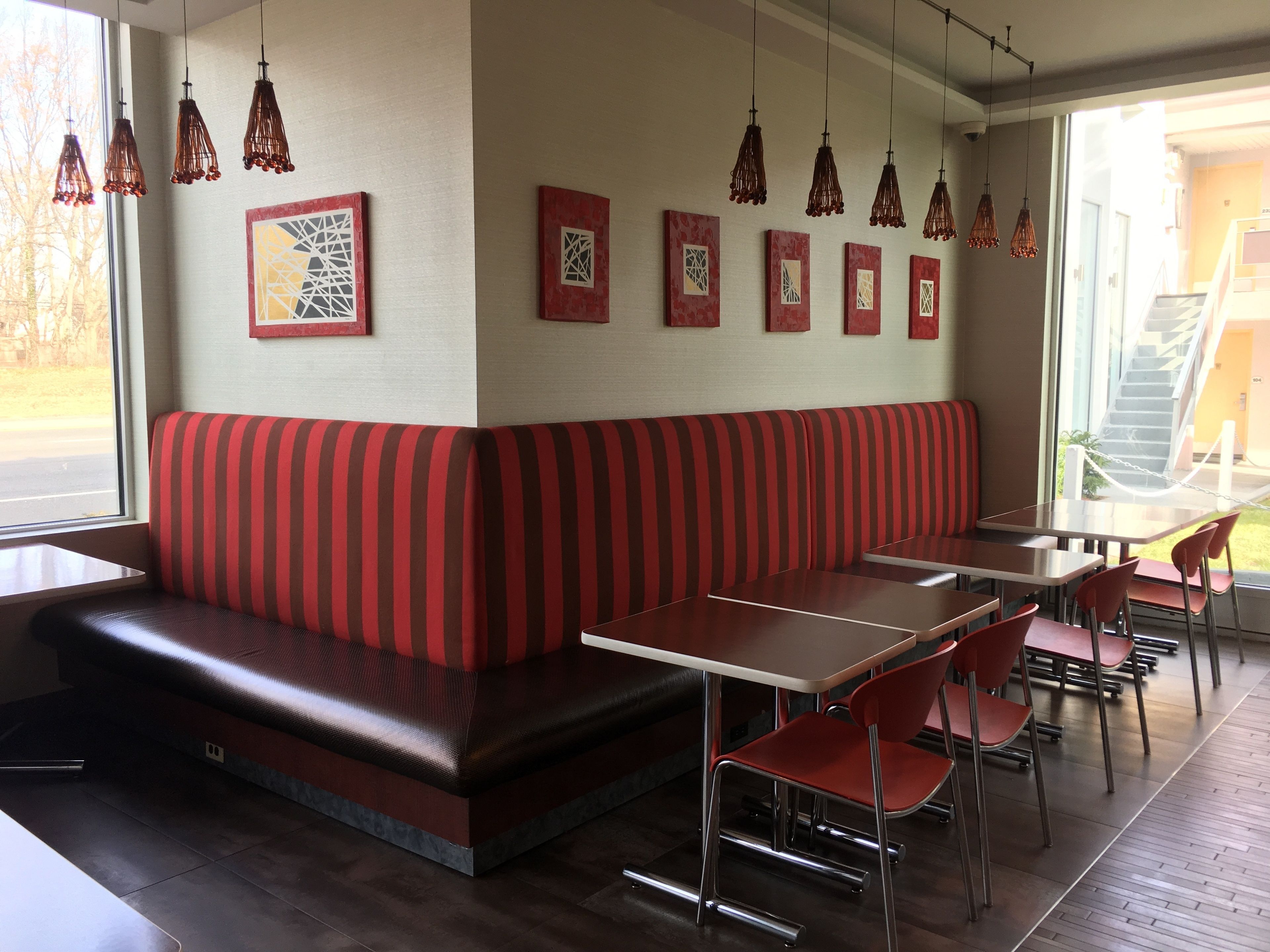 A restaurant with a red-striped booth, multiple tables, and hanging pendant lights.