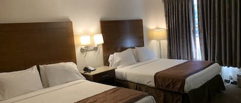 Habitación de hotel con dos camas, una mesita de noche con teléfono, lámparas de pared y una ventana con cortinas.