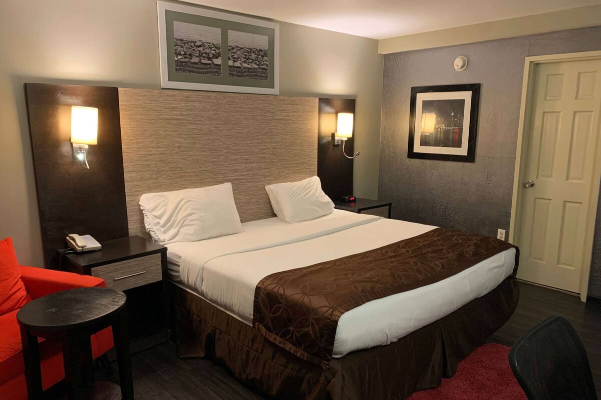 A hotel room with a bed, bedside tables, a chair, a desk, and a door.