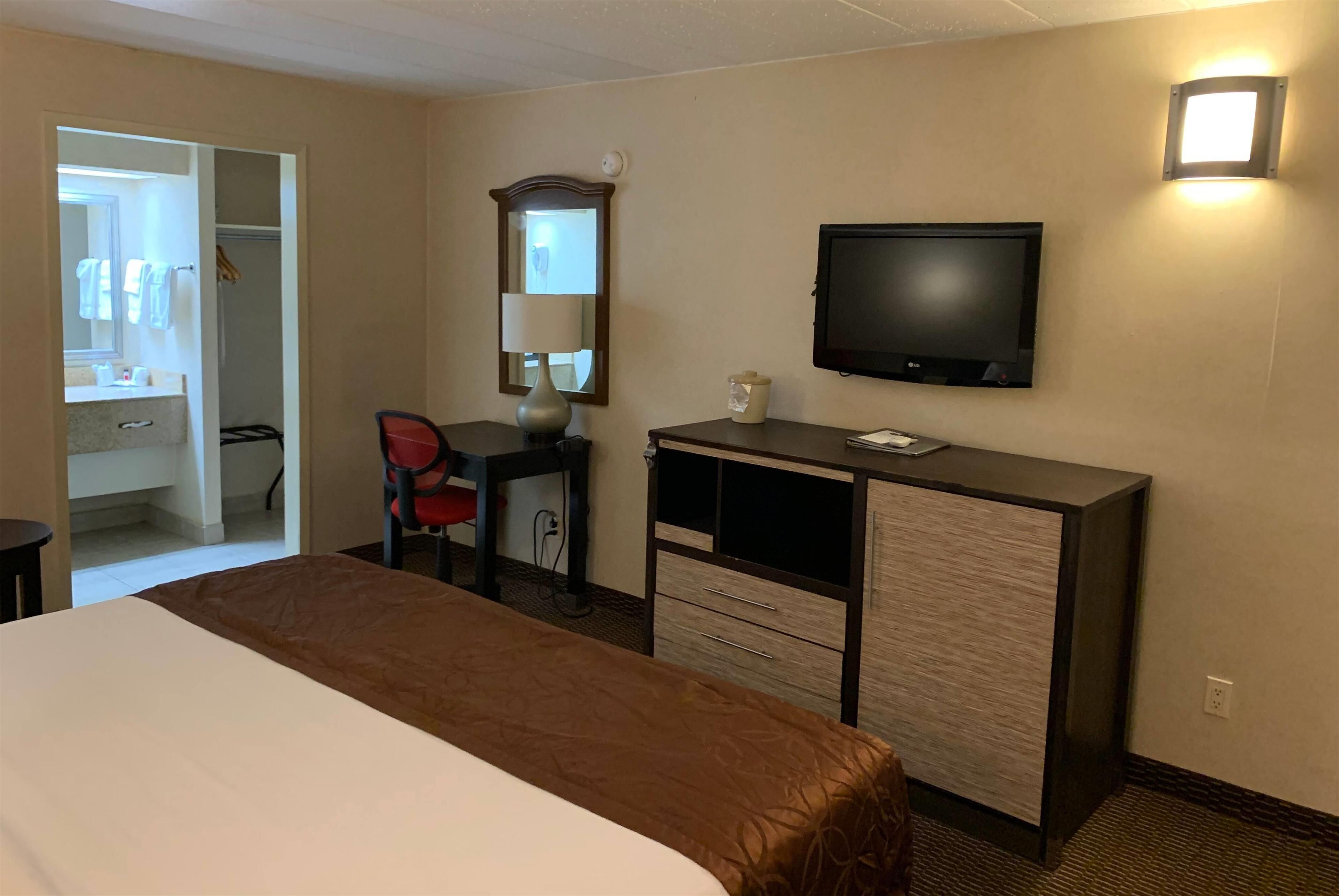 A hotel room with a bed, a desk, a chair, a television, and a mirror.