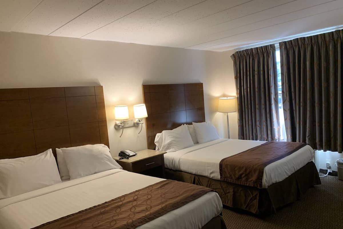A hotel room with two beds, a nightstand with a phone, wall-mounted lamps, and a window with curtains.
