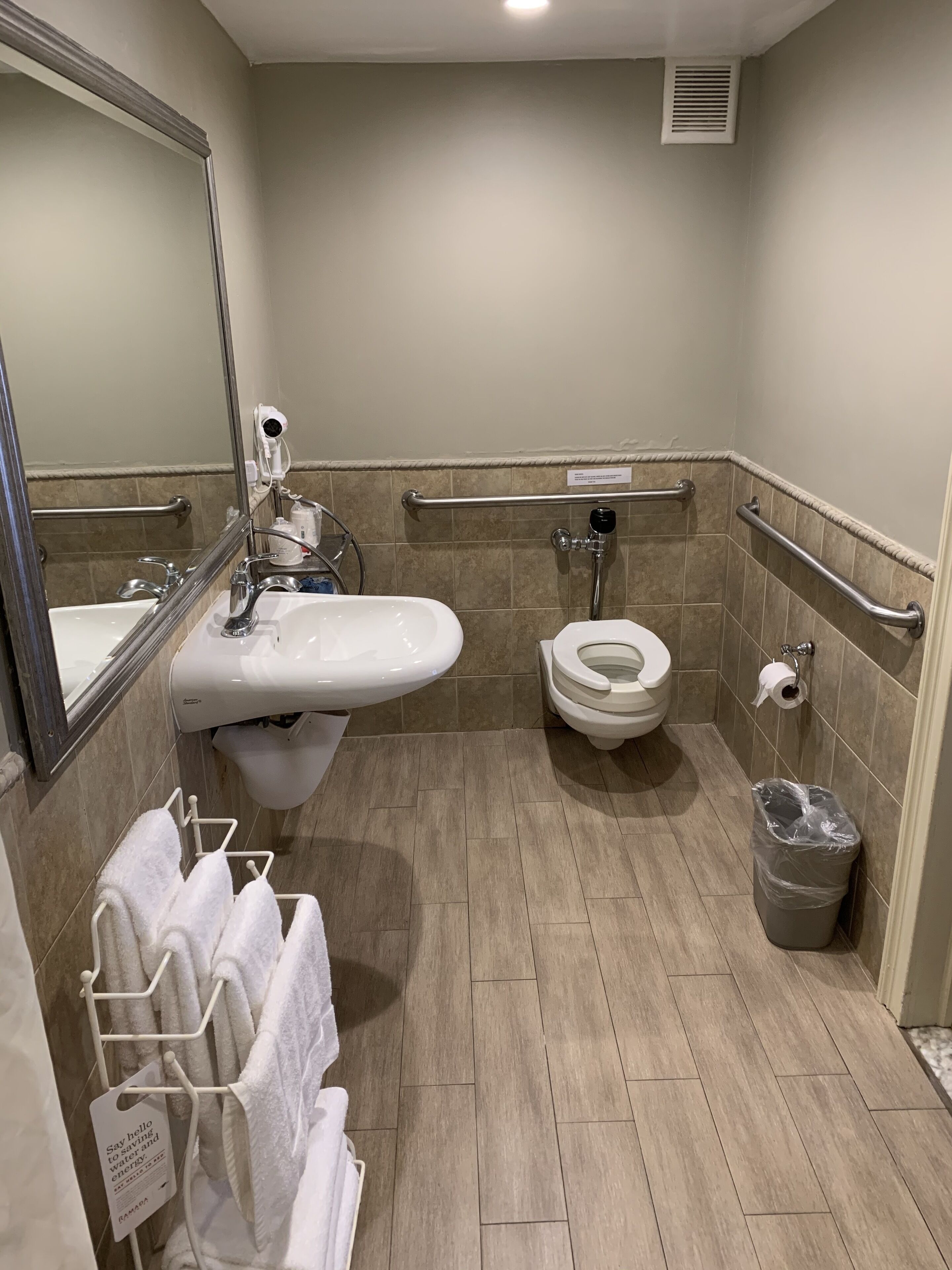 A modern bathroom with a sink, toilet, and hand dryer. There are grab bars and a trash can.