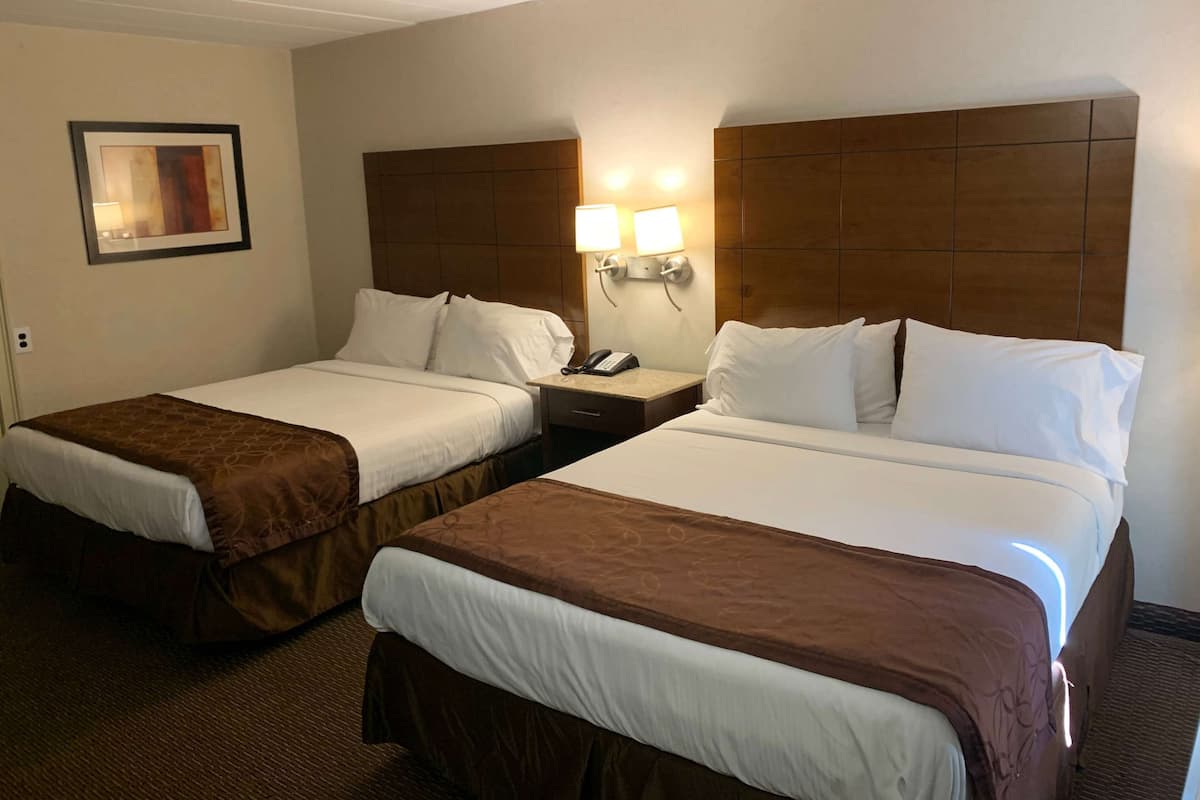 A hotel room with two beds, each with a brown bedspread, a nightstand with a phone, and wall-mounted lights.