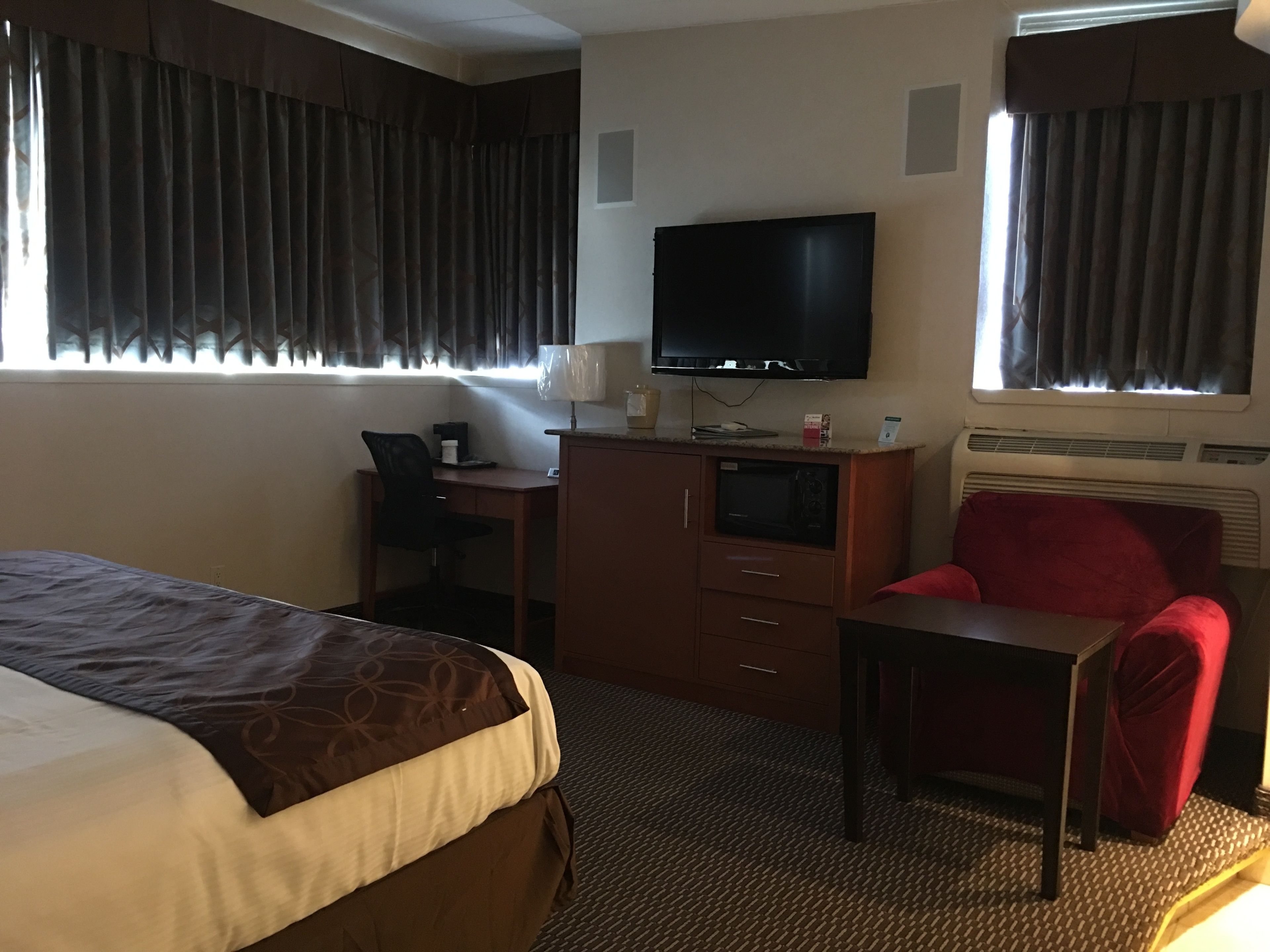 Ein Hotelzimmer mit Bett, Schreibtisch mit Stuhl, Fernseher und einem roten Sessel.