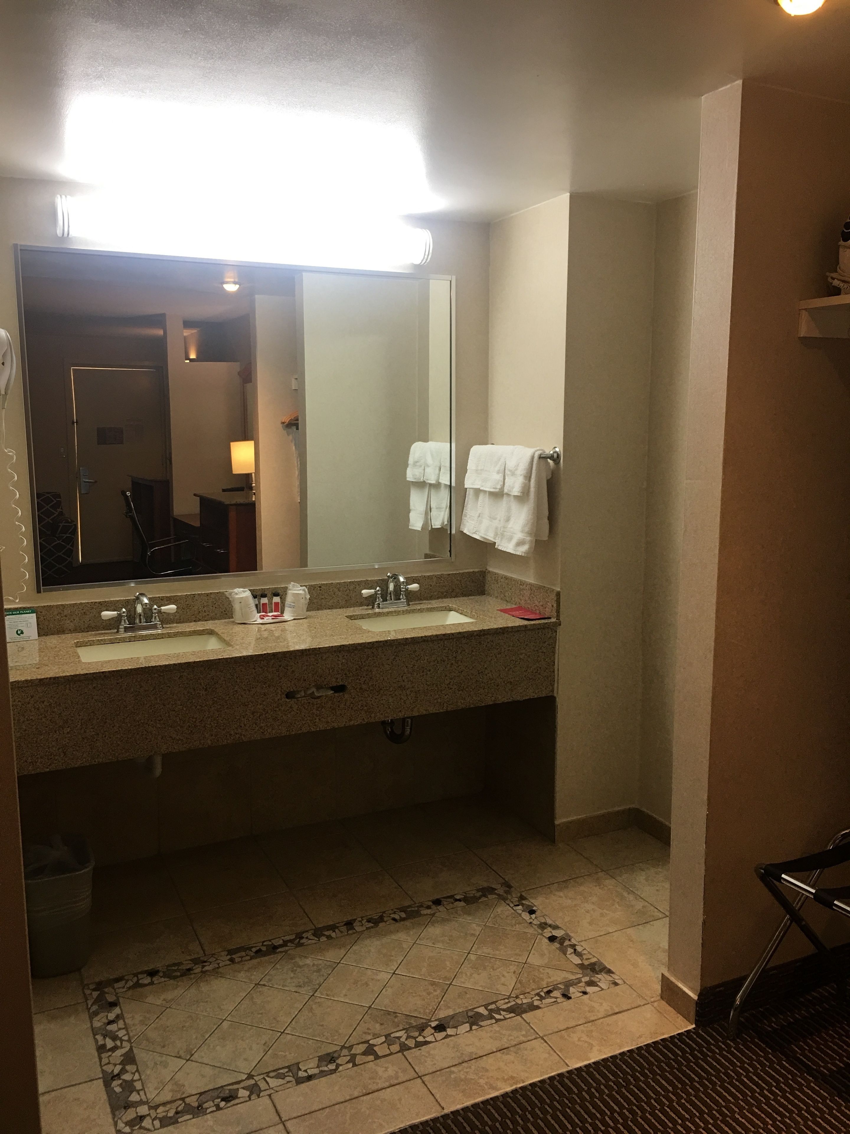 Un baño con un espejo grande, dos lavamanos, un perchero para toallas y una alfombra estampada.