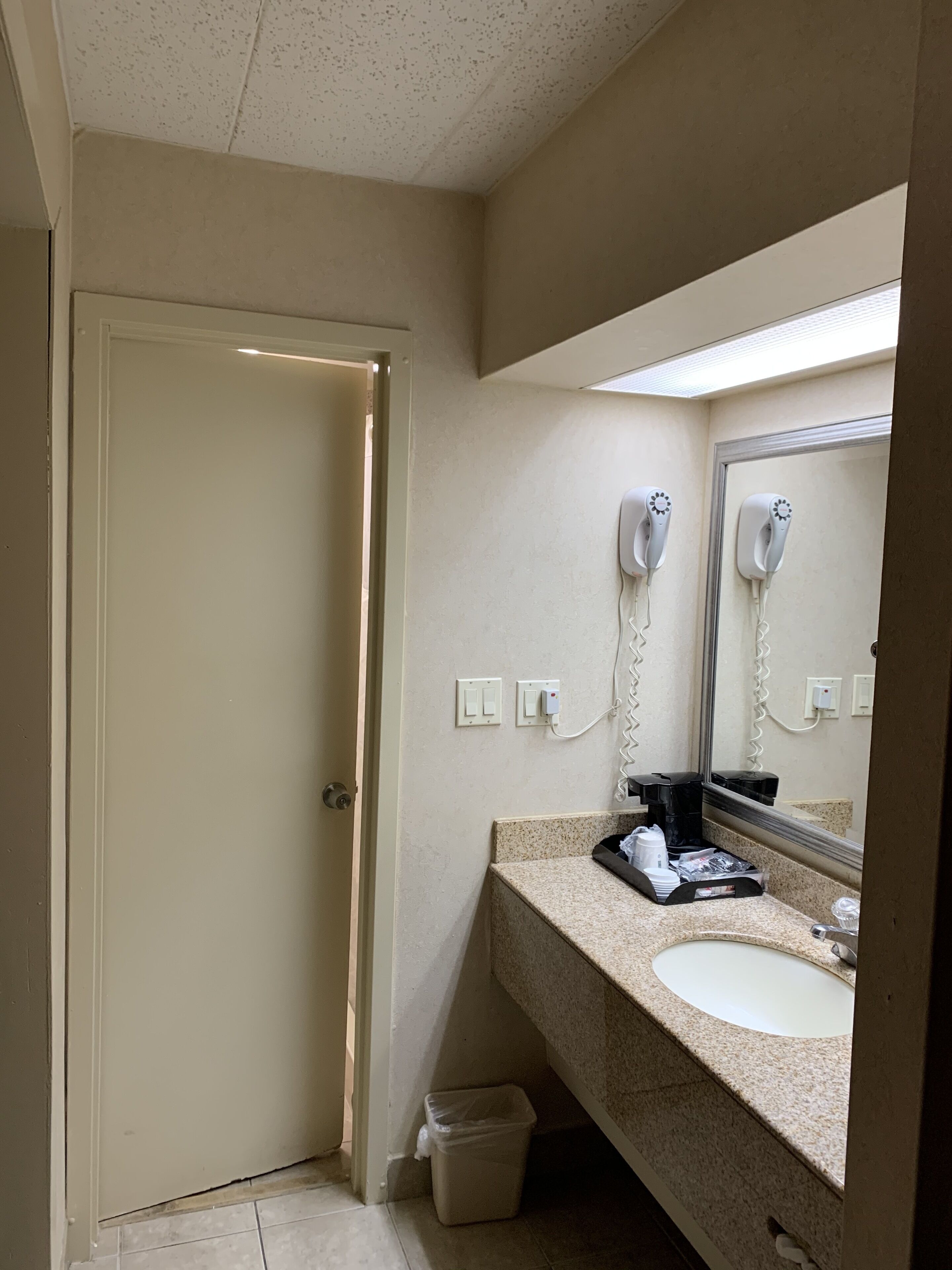 A hotel bathroom with a sink, mirror, hairdryer, and coffee maker.