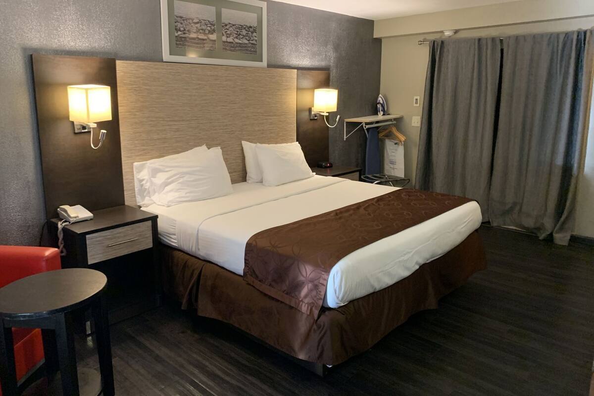 A hotel room with a bed, bedside lamps, a telephone, a desk, a chair, and a window with curtains.