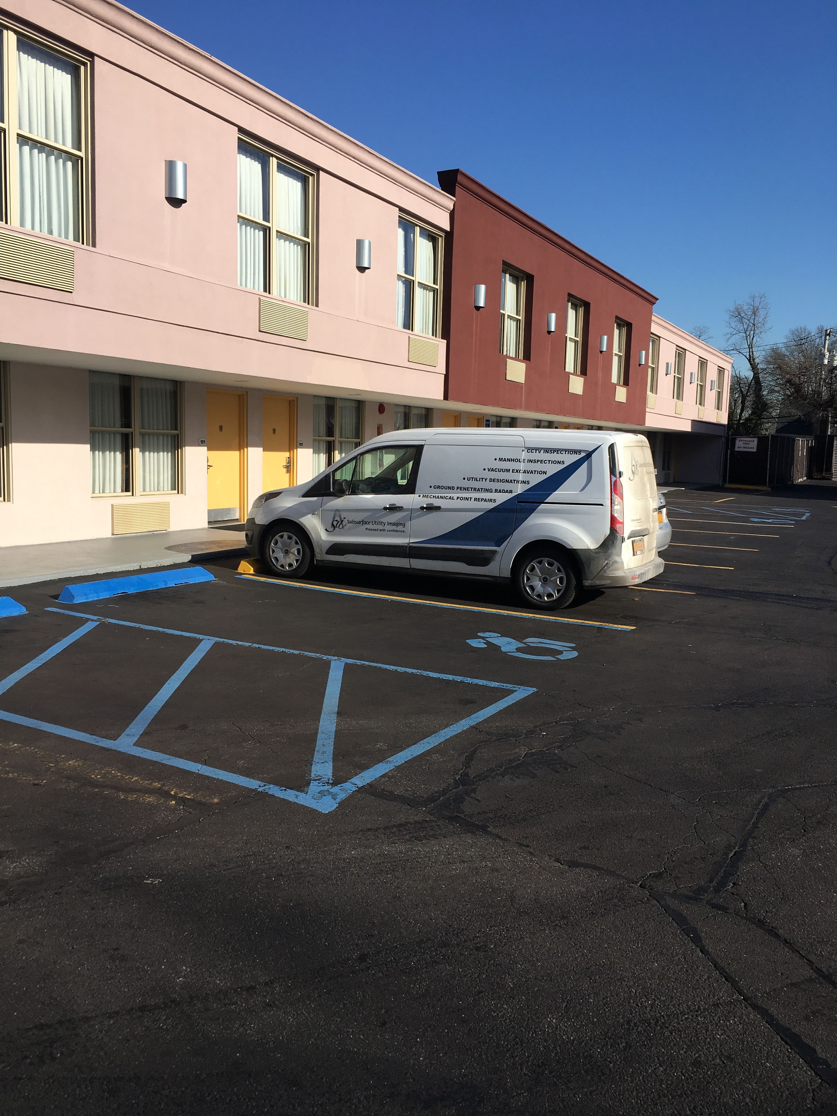 A parking lot with a van parked in front of a building with a pink facade and a yellow door.