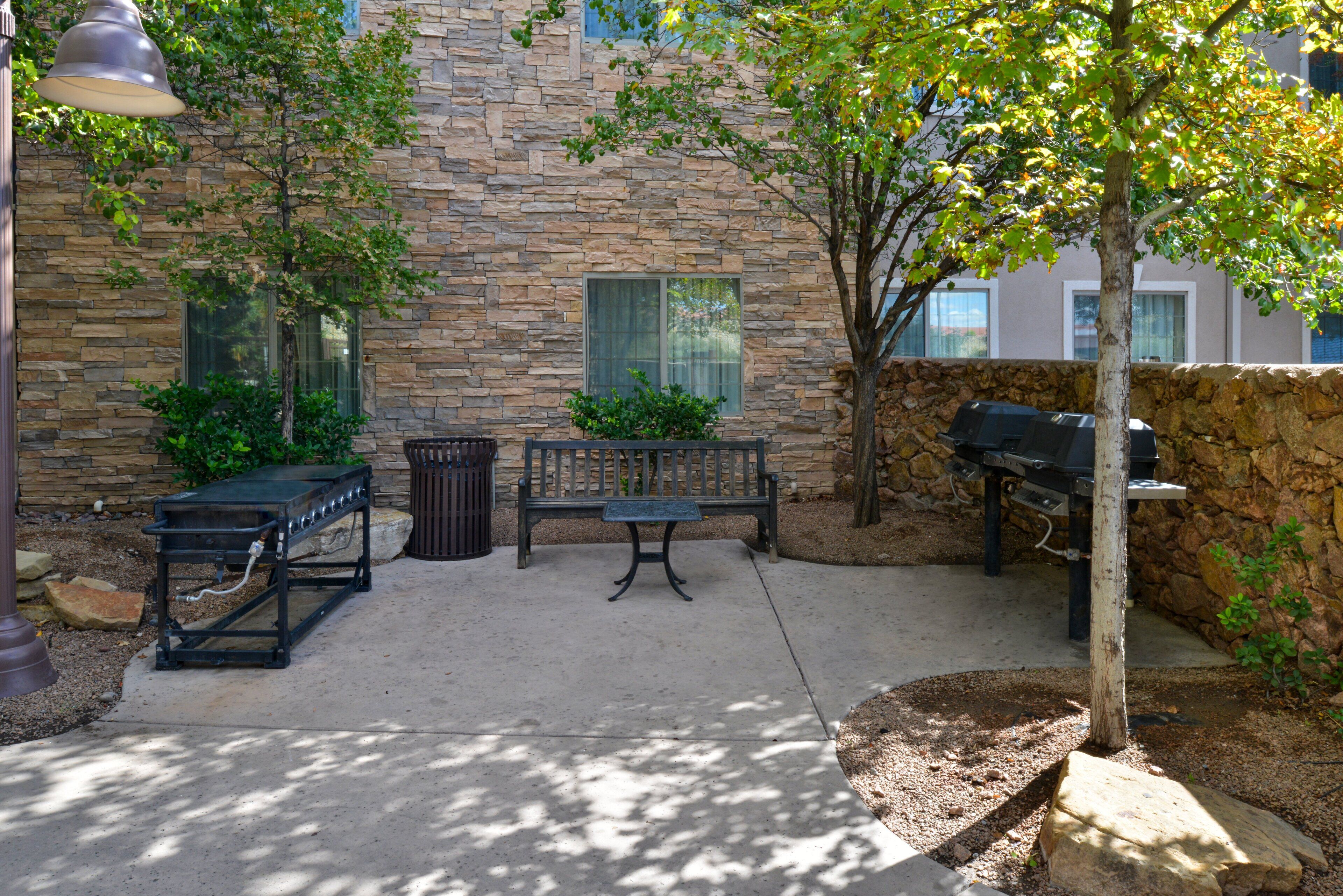 A patio area with a stone wall, a bench, a grill, and a lamp post.