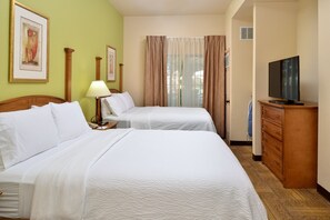 A hotel room with two beds, a television, a lamp, and a dresser.
