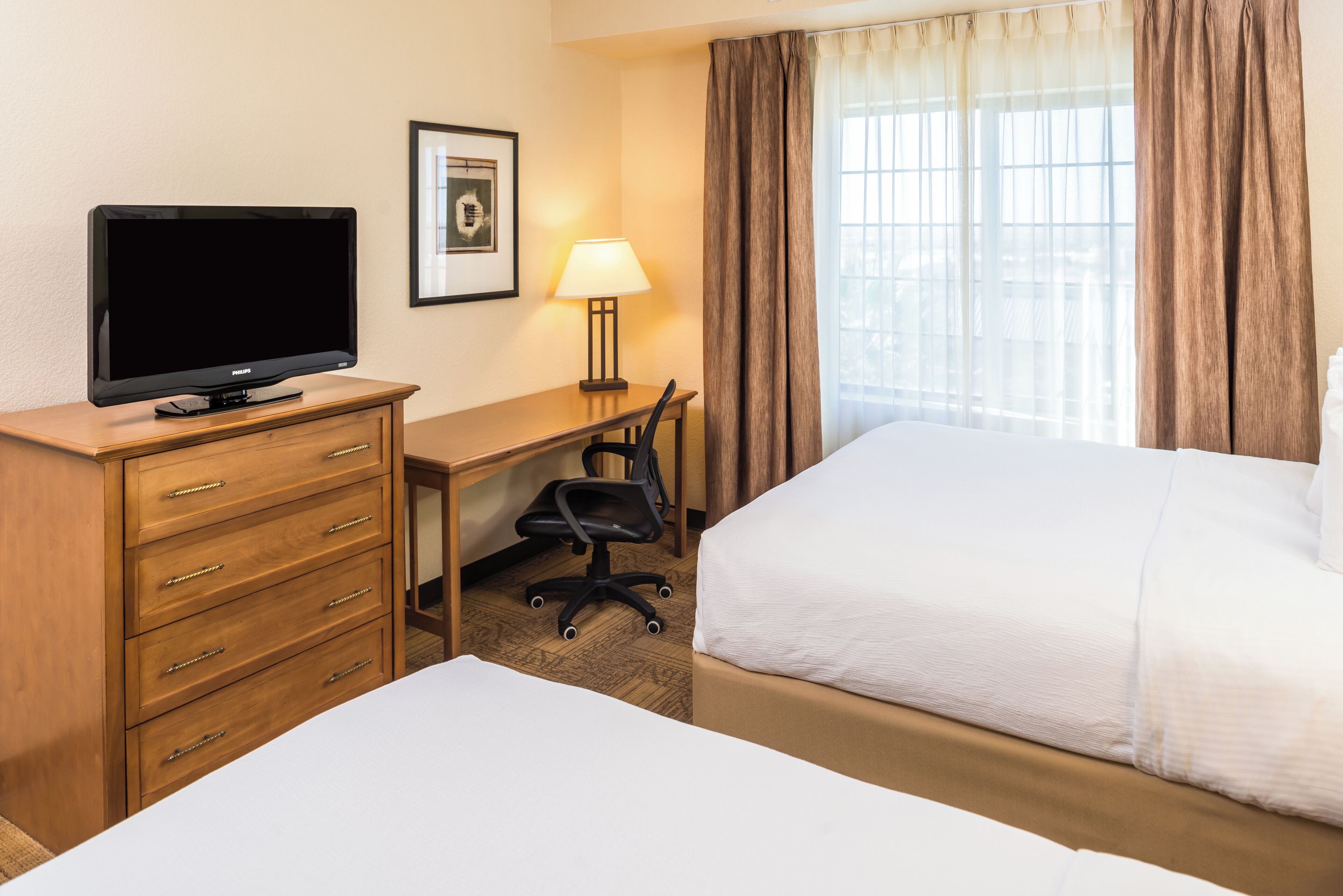 A hotel room with a bed, a desk with a chair, a television, and a lamp.