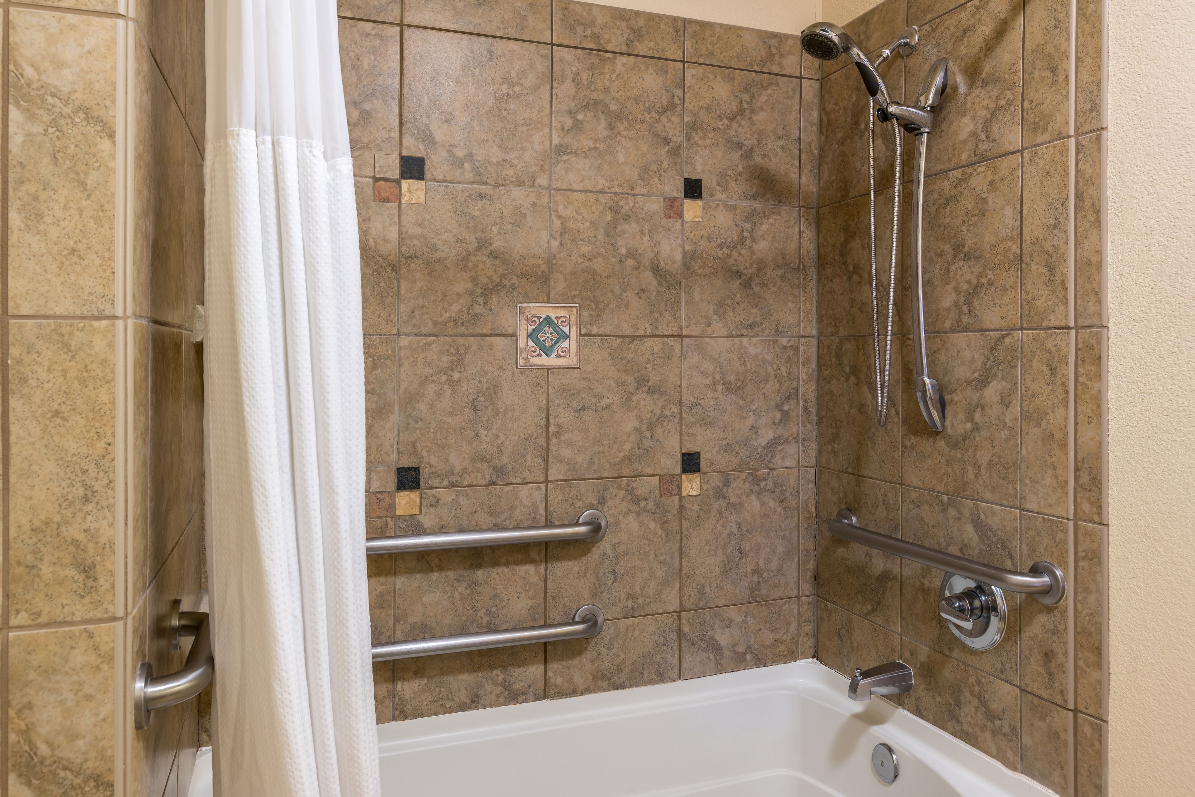 A bathroom with a bathtub, grab bars, a showerhead, and a towel rack.