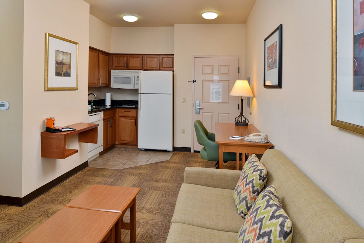 A compact living space with a kitchenette, a sofa with patterned cushions, a small table, and a lamp.