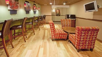 A restaurant with wooden flooring, red patterned chairs, and a TV mounted on the wall.