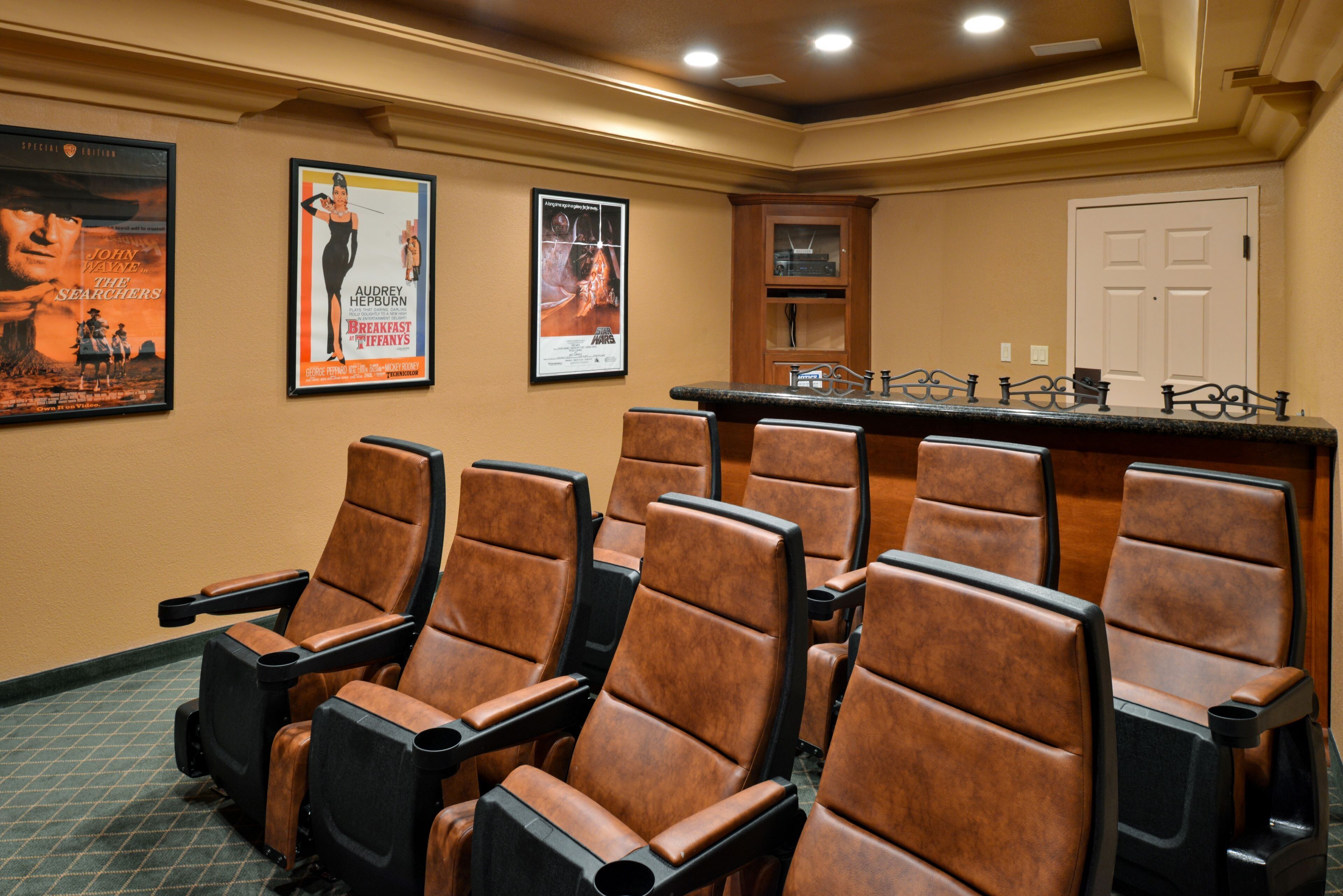 A cinema room with rows of brown leather seats, a bar area, and two movie posters on the wall.