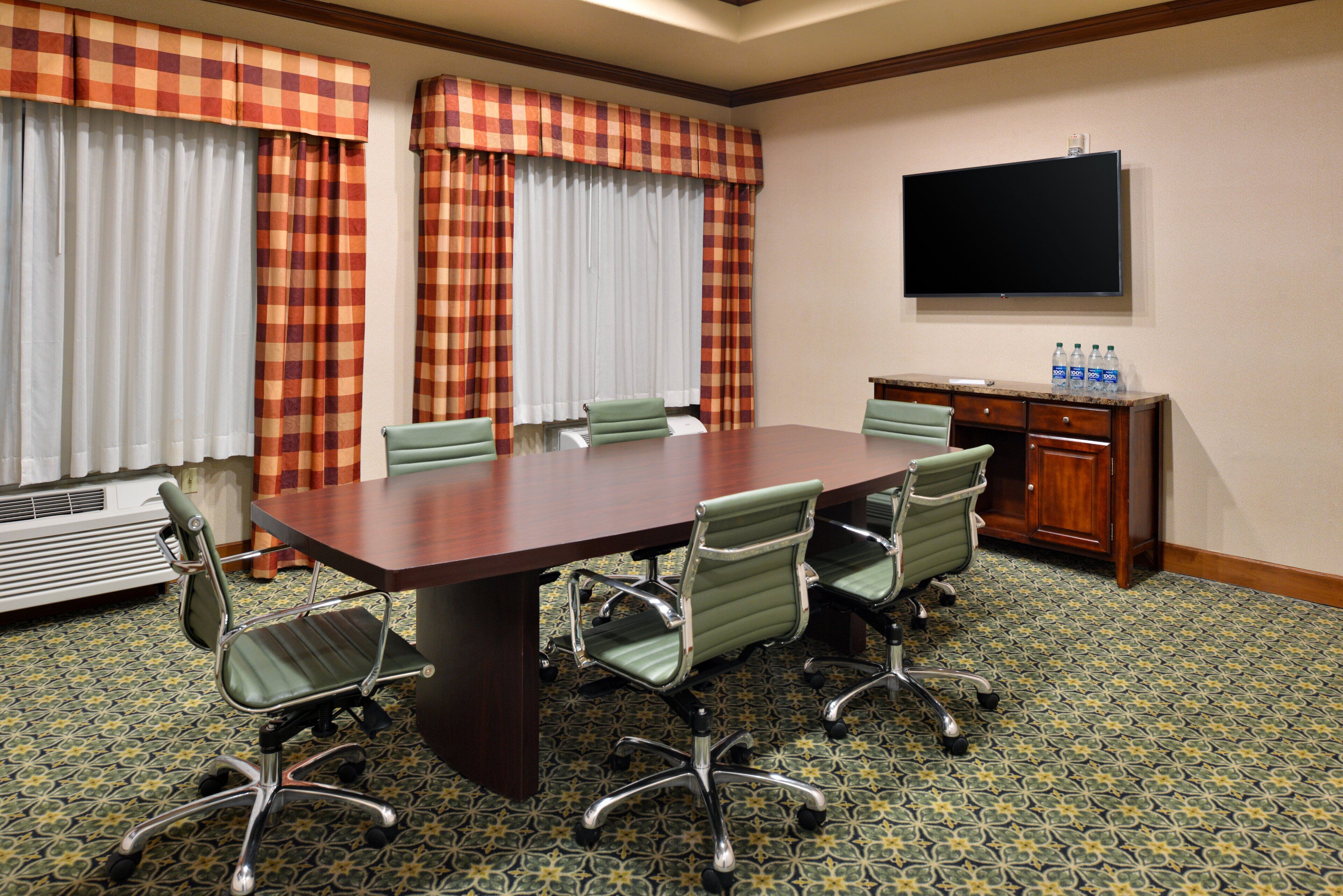 A conference room with a large table, four chairs, a television, and a water dispenser.