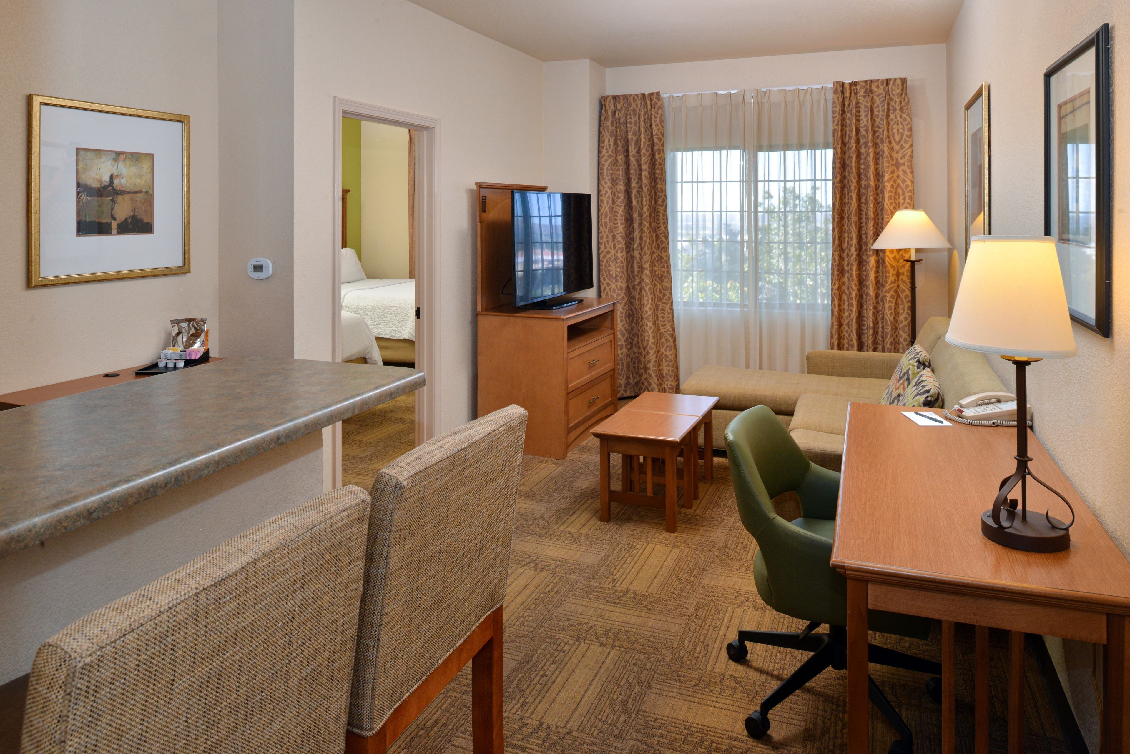 Ein Hotelzimmer mit Küchenzeile, Fernseher, Sofa, Schreibtisch und einer Lampe.