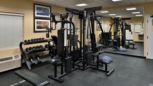 Un gimnasio con diferentes máquinas de ejercicio, mancuernas y bancos.