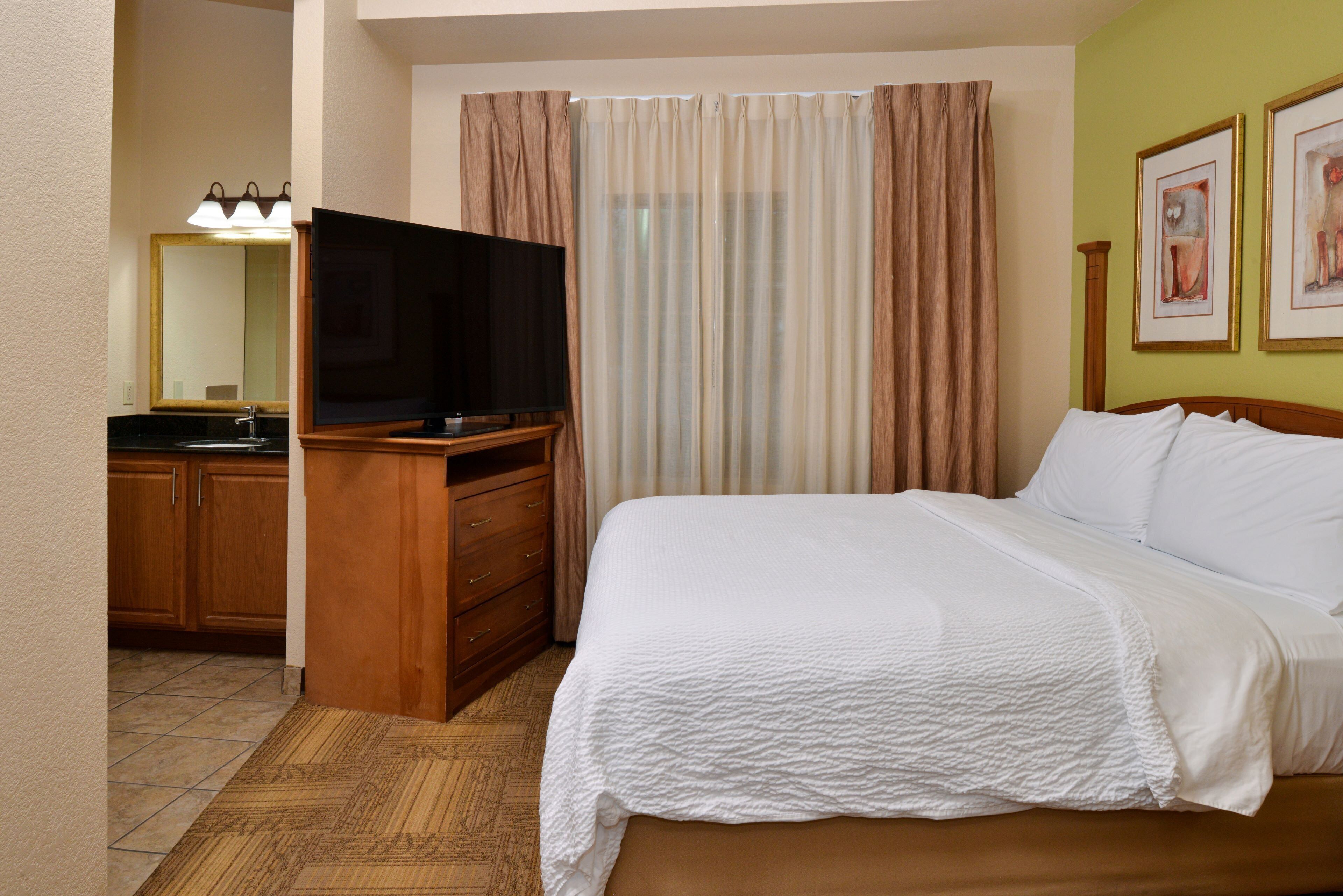 A hotel room with a bed, a TV, a bathroom with a sink, and curtains.