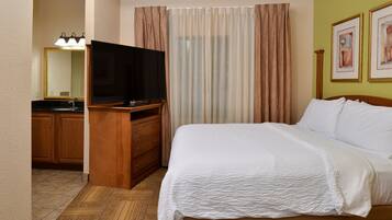 A hotel room with a bed, a TV, a bathroom with a sink, and curtains.